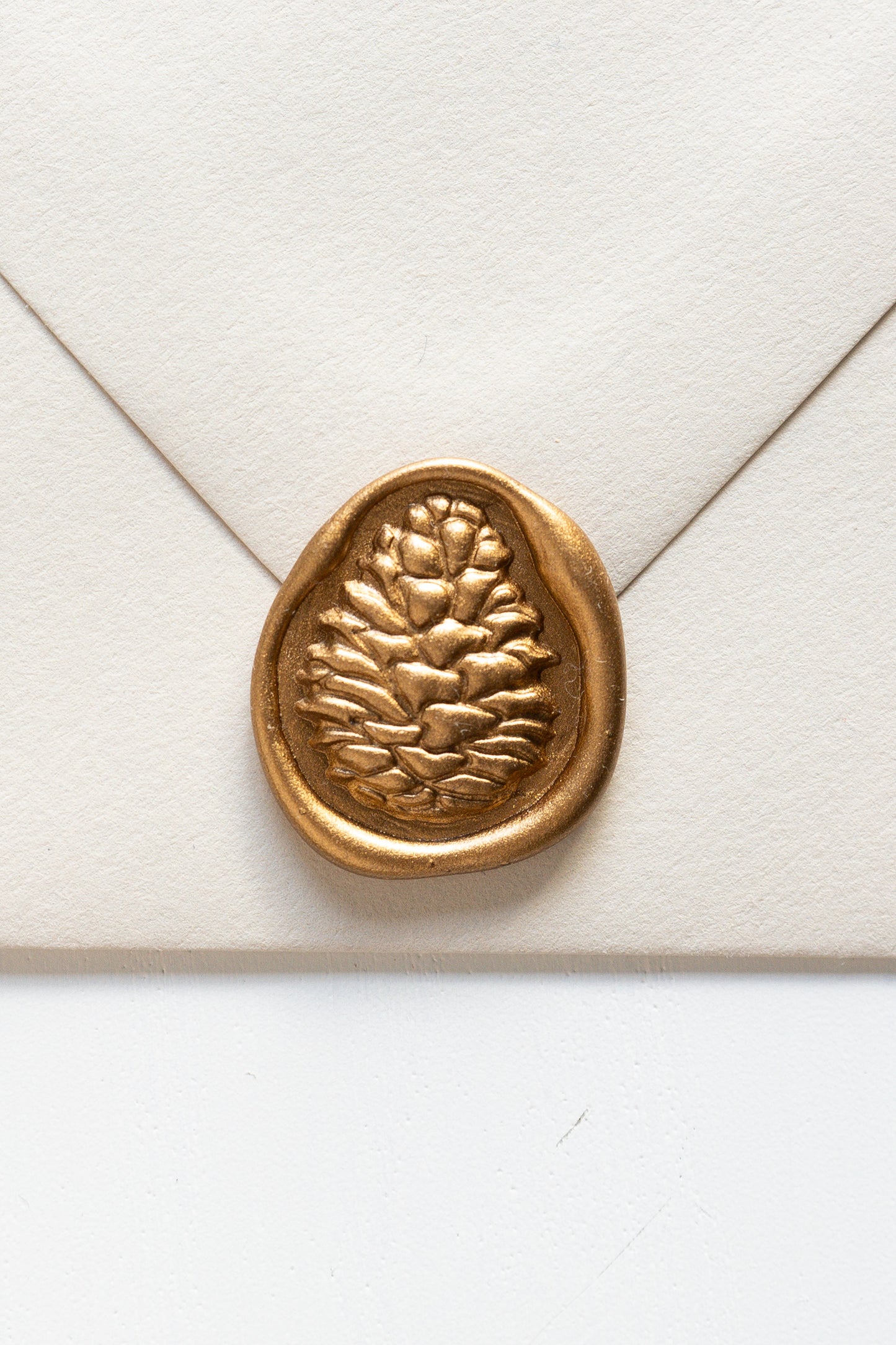 A beige envelope featuring a golden 3D pinecone wax seal, perfect for Holiday greeting cards