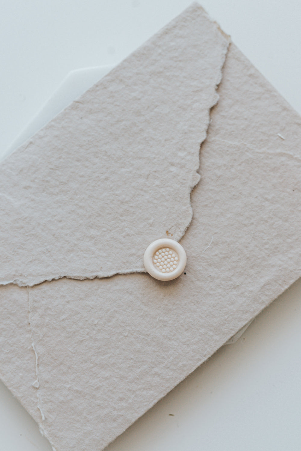 A mini 9mm blush wax seal with a 3D bubble waffle design on a textured taupe envelope