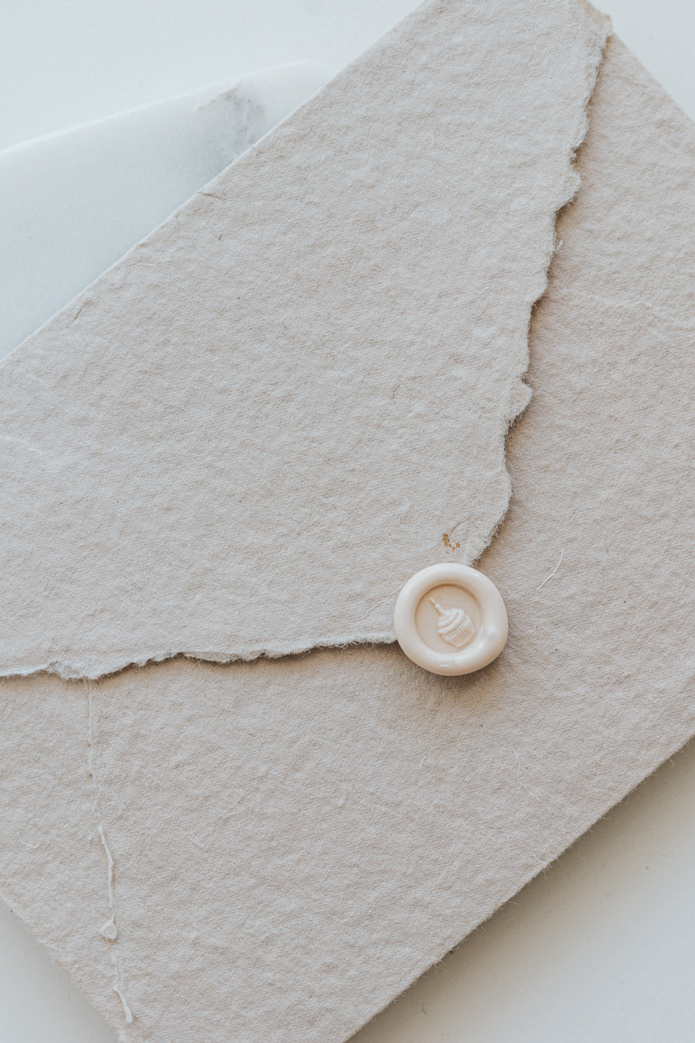 A mini 9mm blush wax seal with a 3D French fries design on a textured taupe envelope