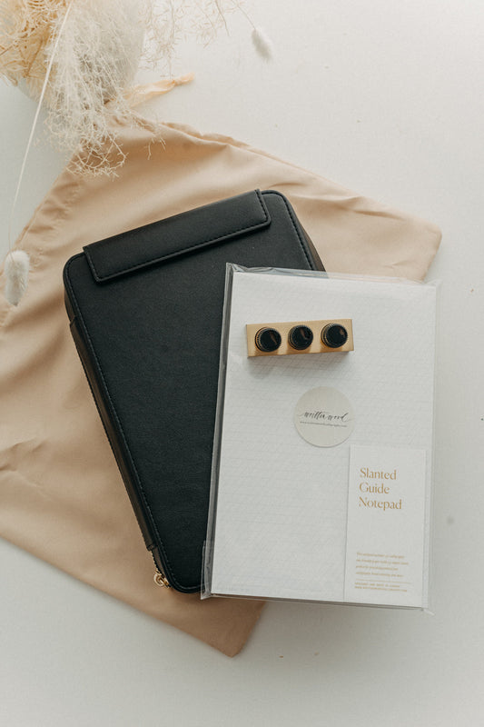 Black travel kit on a beige dust bag with a slanted guide notepad and mini tilted inkwell on a white surface