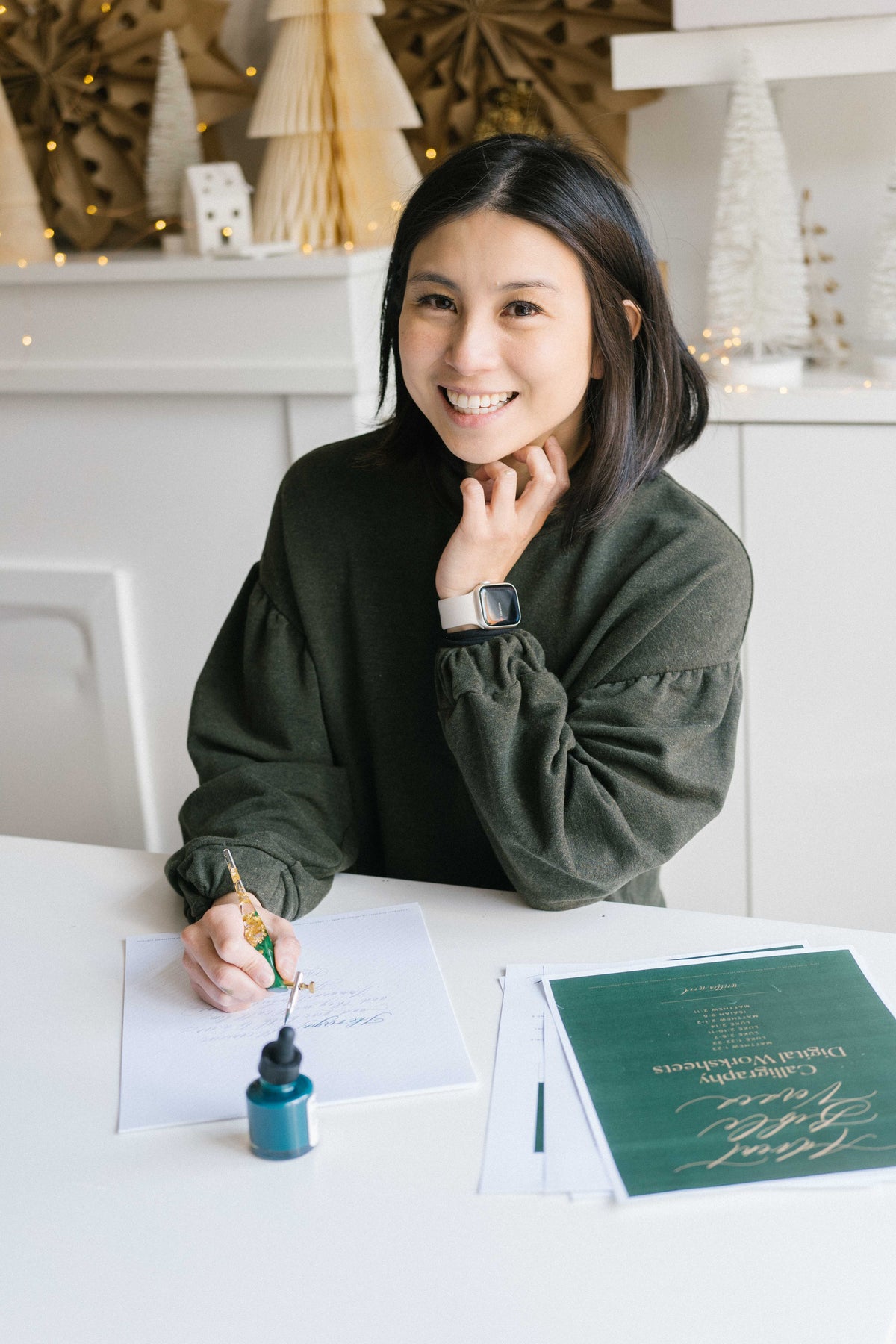 Woman smiling while practicing calligraphy with oblique pen and ink at desk with worksheets and stationery