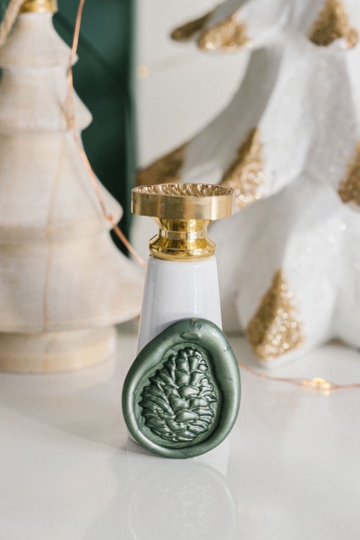 Green wax seal impression of a pinecone with brass stamp on marble surface with festive holiday decor background