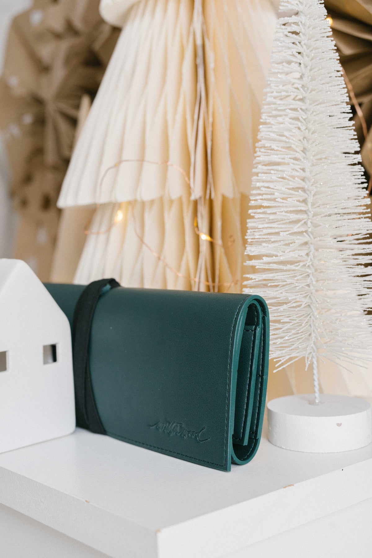 Green vegan leather calligraphy pen roll case on shelf with neutral Christmas decor and paper trees