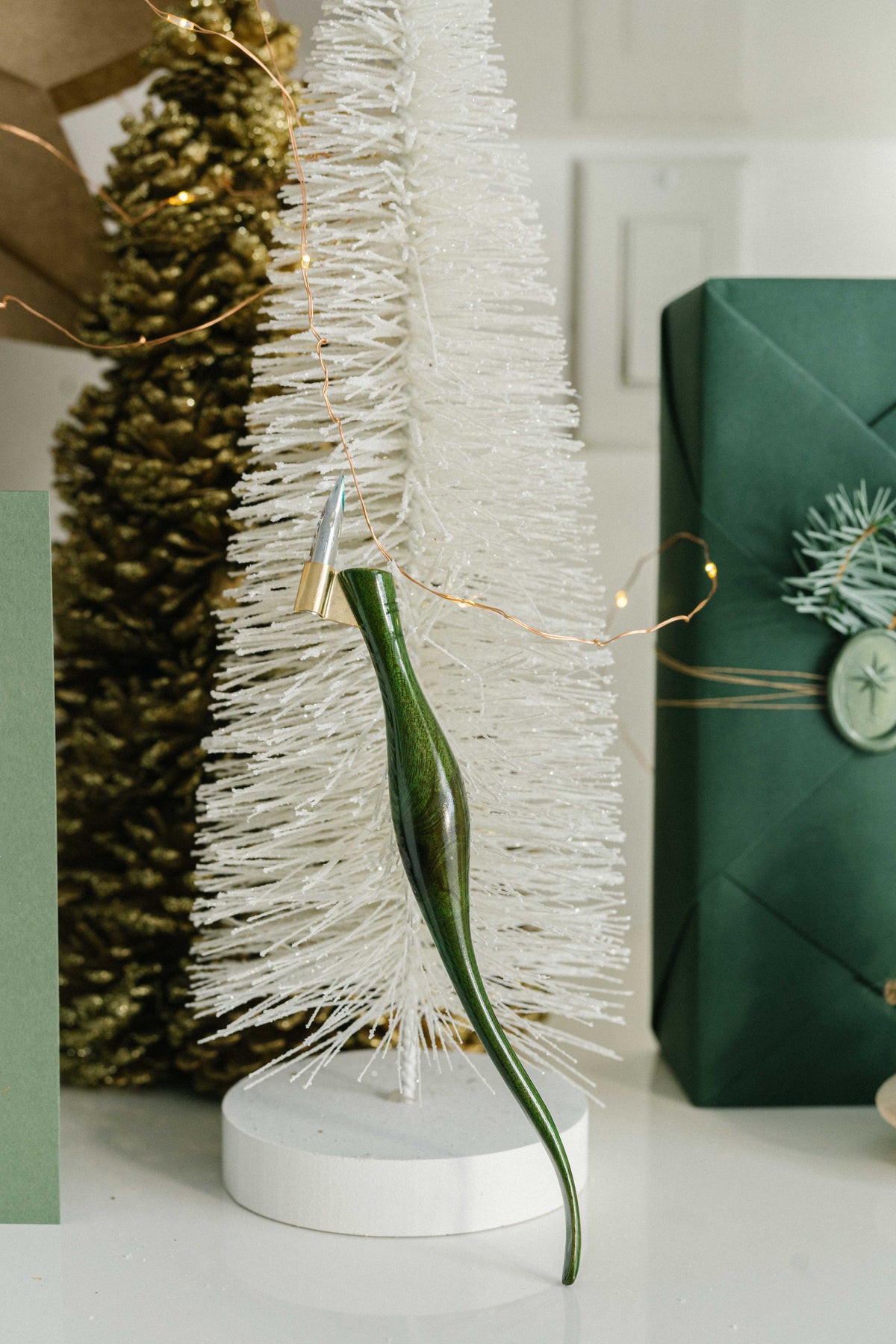 Green oblique calligraphy pen displayed on white Christmas tree with warm lights and holiday decor