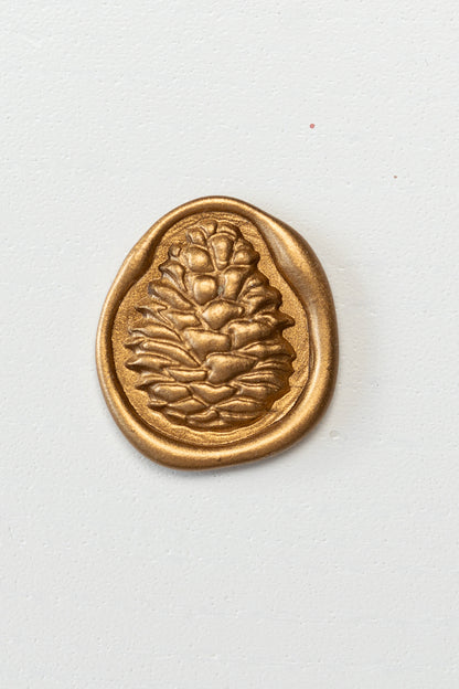 A golden 3D pinecone wax seal on a white surface