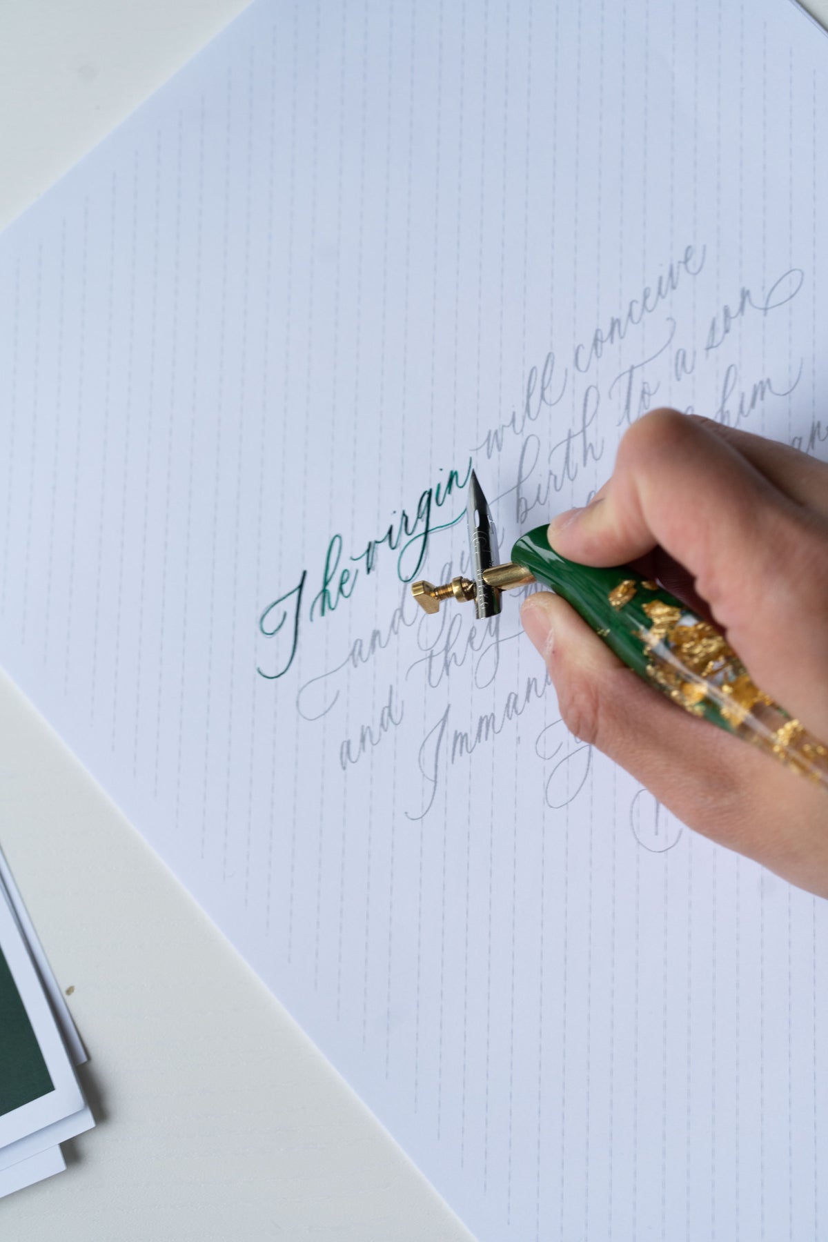 Close-up of oblique calligraphy pen writing green ink lettering on practice sheet for modern calligraphy