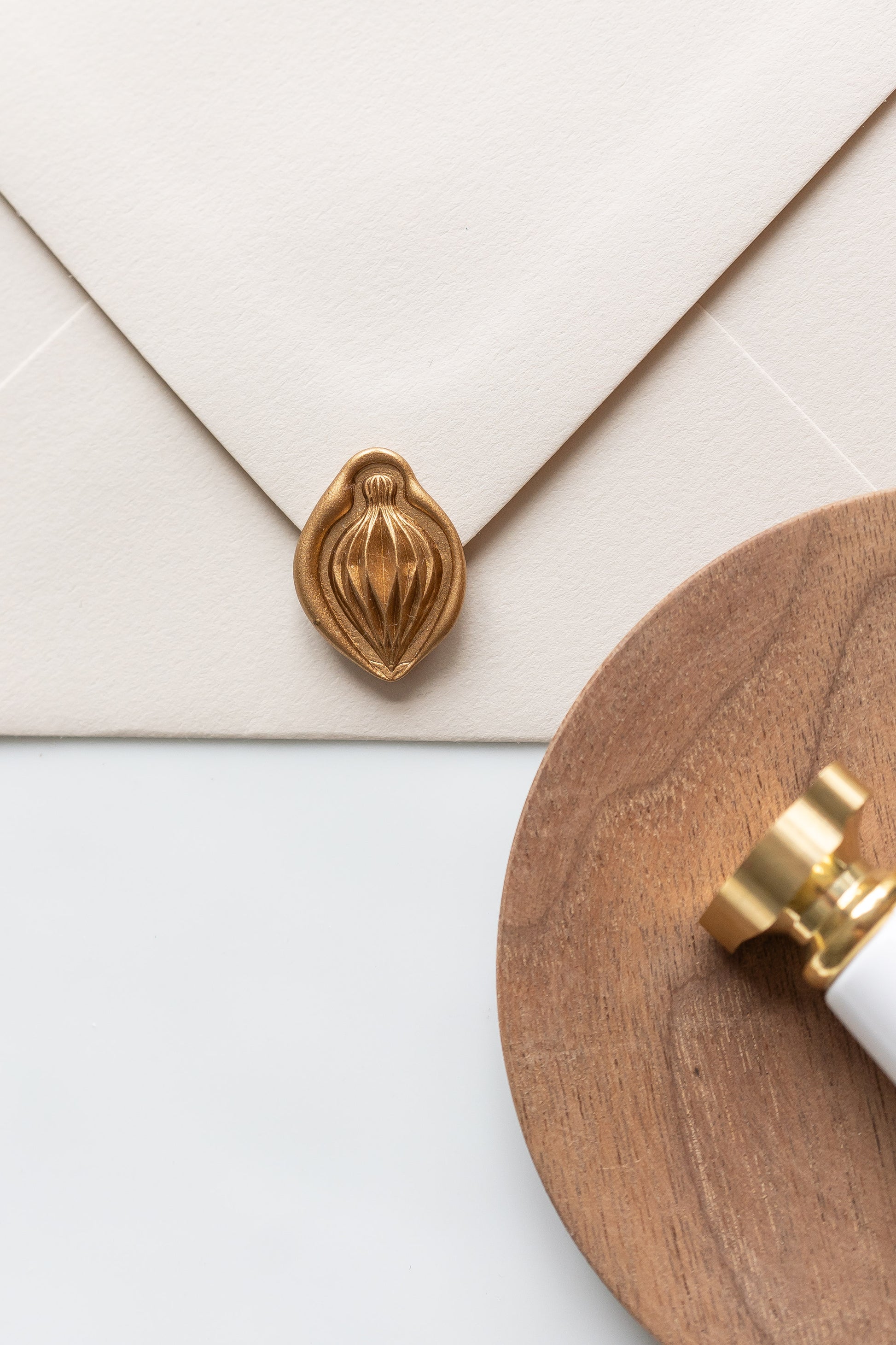 A wax seal stamp and beige envelope showcasing a gold paper ornament wax seal, perfect for Holiday greeting cards
