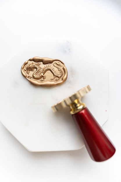 A gold Lunar New Year wax seal featuring an ancient dragon design, with a brass stamp and wooden handle