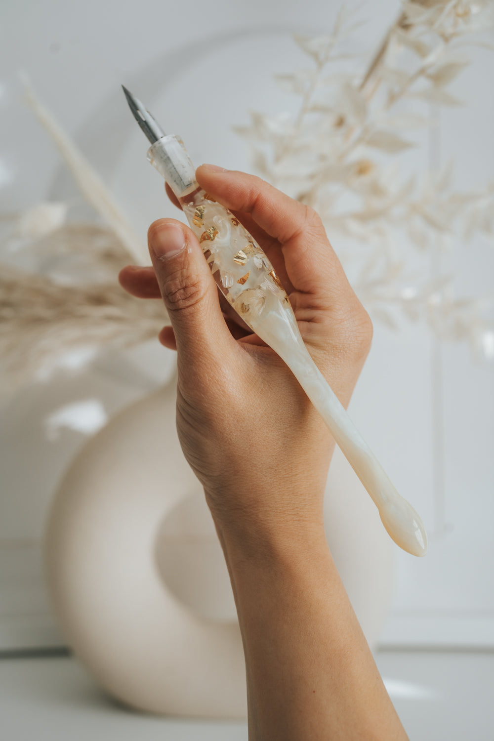 Hand holding ivory resin calligraphy pen with gold flakes, aesthetic modern calligraphy penholder