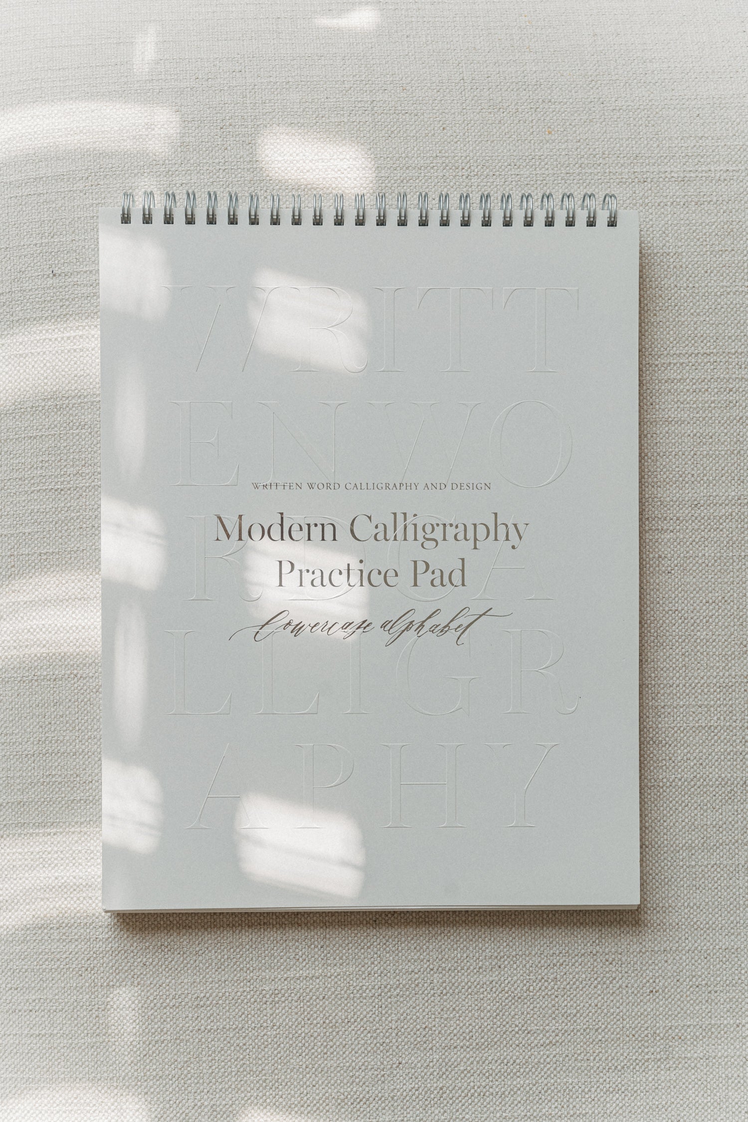 Modern Calligraphy Practice Pad for lowercase alphabet on a textured surface, with light shadows creating a minimalist aesthetic