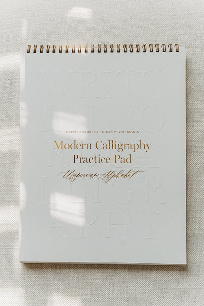 Modern calligraphy practice pad featuring an uppercase alphabet, with a gold spiral binding
