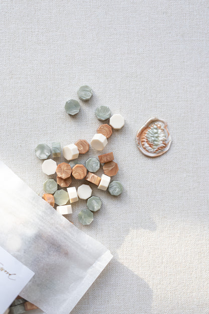 Close-up of Cozy Pine wax seal beads with sage, ivory, and metallic copper colors beside finished wax seal impression