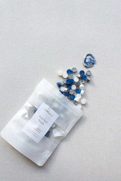 Starry night wax seal beads in blue, silver and white mix spilling from pouch on neutral linen background