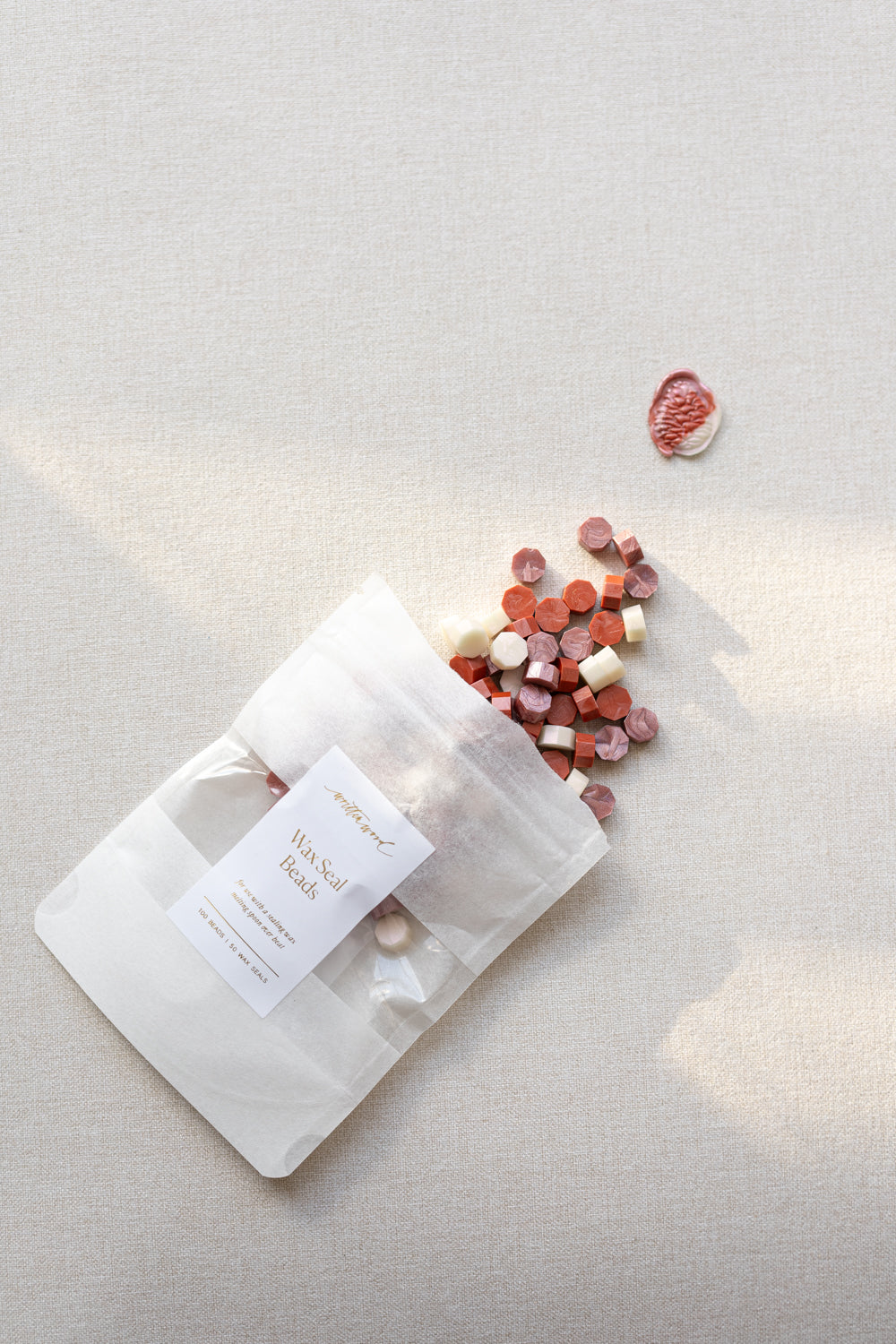 Wax seal beads in frosted blush color mix in labeled pouch with scattered beads and finished seal on linen surface