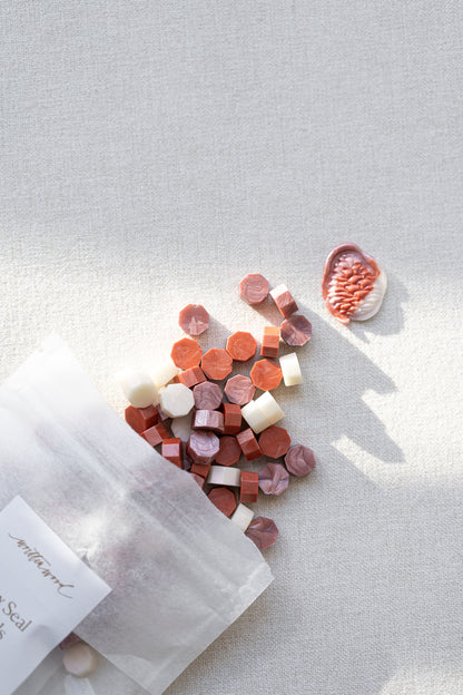 Frosted blush wax seal beads spilled from pouch with soft pink, coral and cream tones on neutral linen background