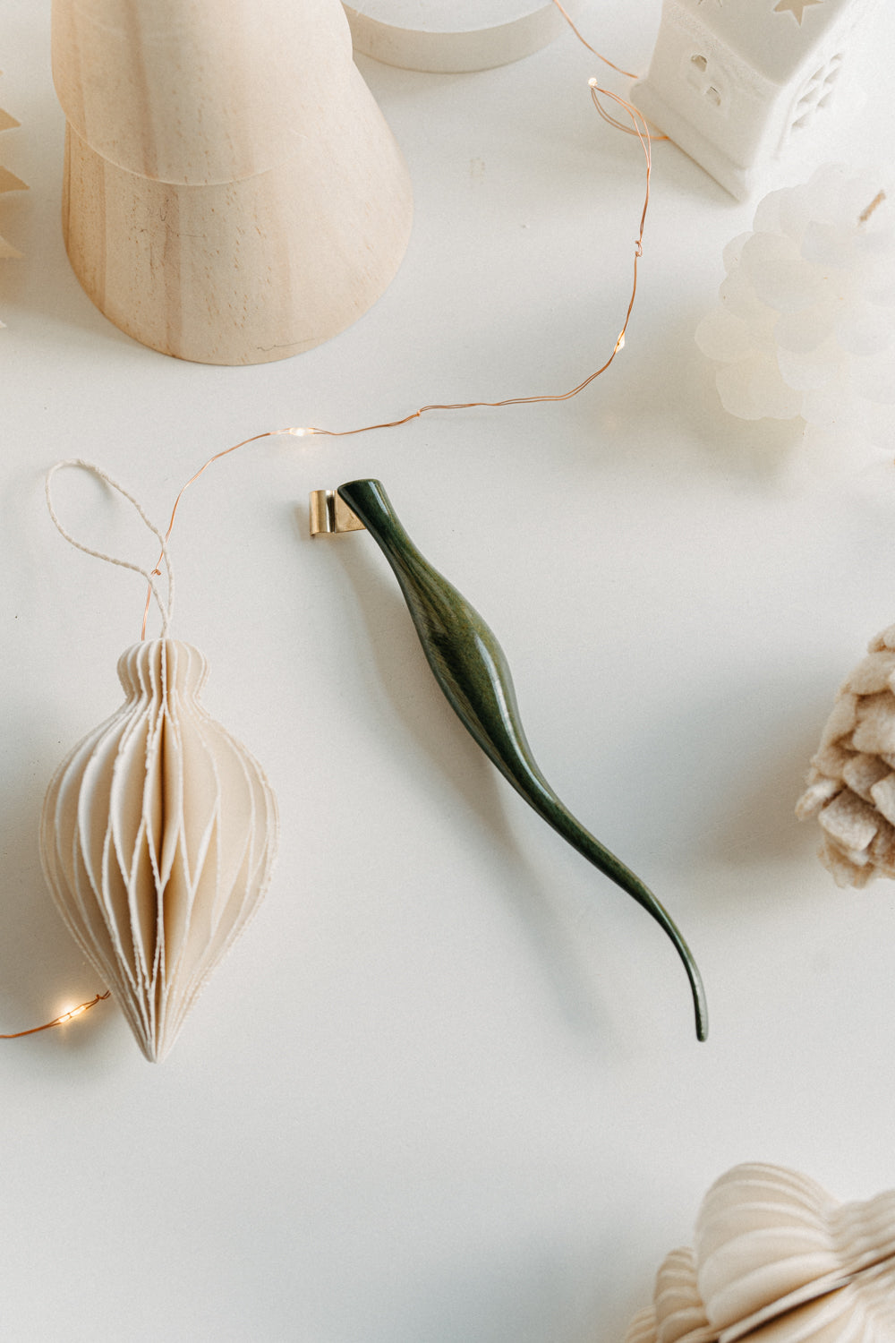 Handcrafted curved green lacquer calligraphy penholder resting on a white desk with soft holiday decorations and warm twinkle lights.
