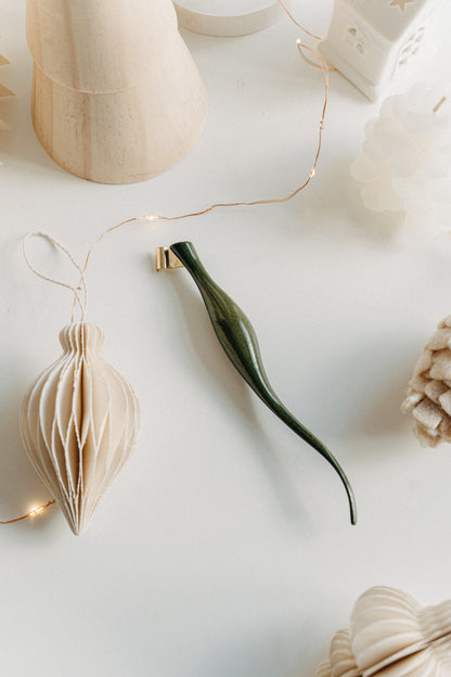 Handcrafted curved green lacquer calligraphy penholder resting on a white desk with soft holiday decorations and warm twinkle lights.
