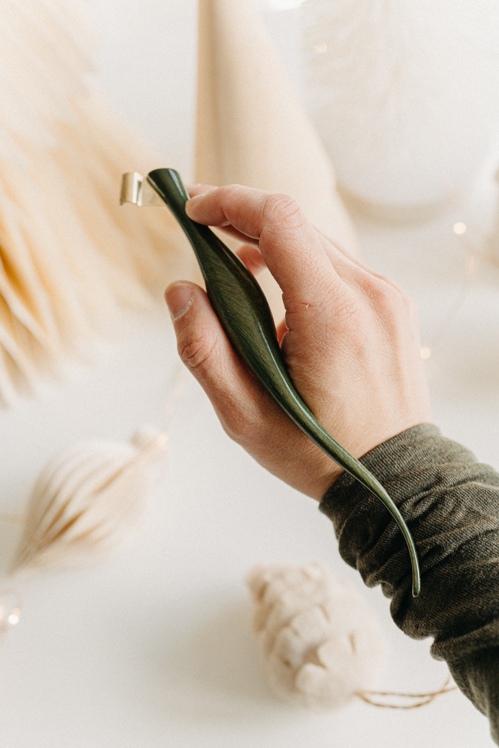 Hand holding a handcrafted curved green lacquer wooden calligraphy penholder, surrounded by warm neutral holiday decorations.