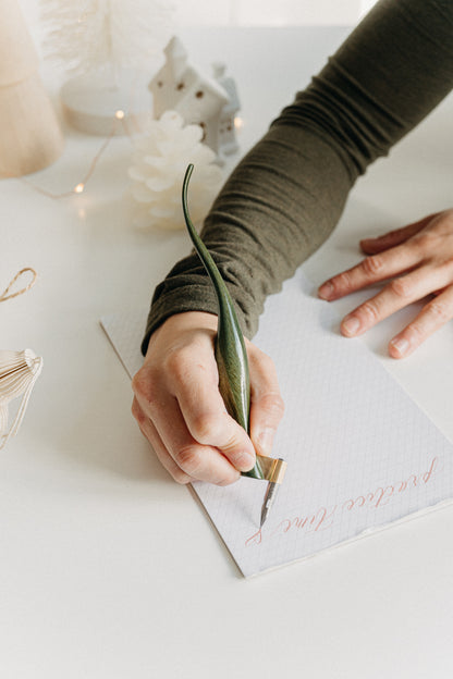Writing “practice time” with a handcrafted green lacquer curved calligraphy penholder in a cozy holiday setting.