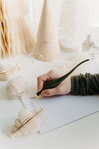 Handwriting with a handcrafted curved green lacquer wooden calligraphy penholder, surrounded by soft holiday décor.