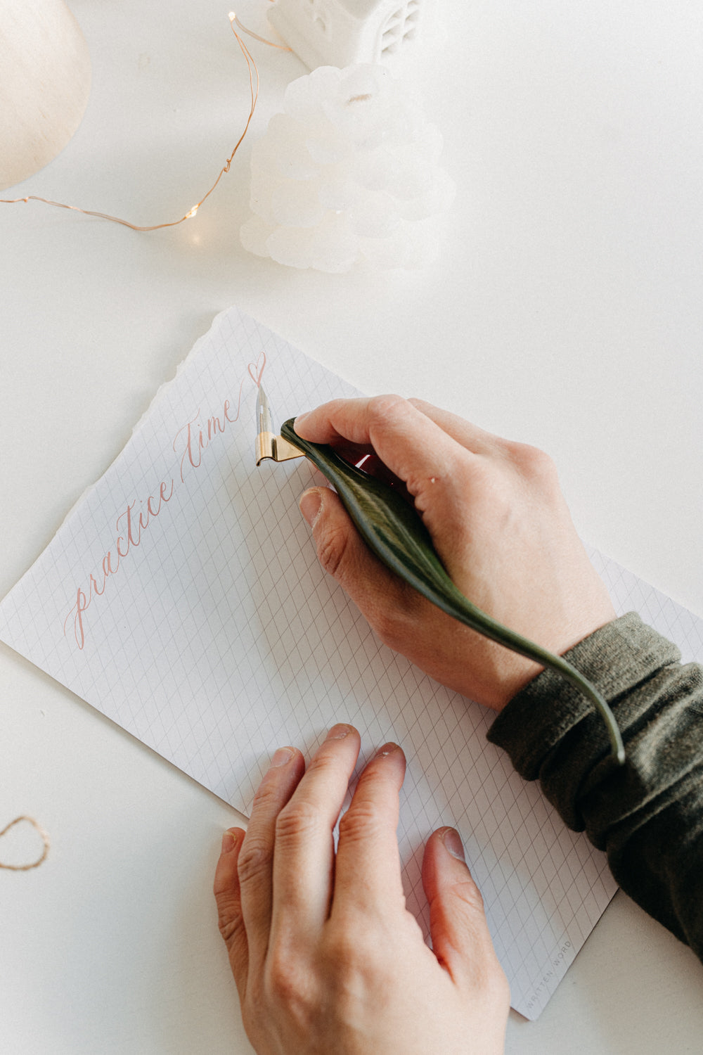 Hand using a handcrafted curved wooden calligraphy penholder painted in green lacquer to write “practice time” on paper.
