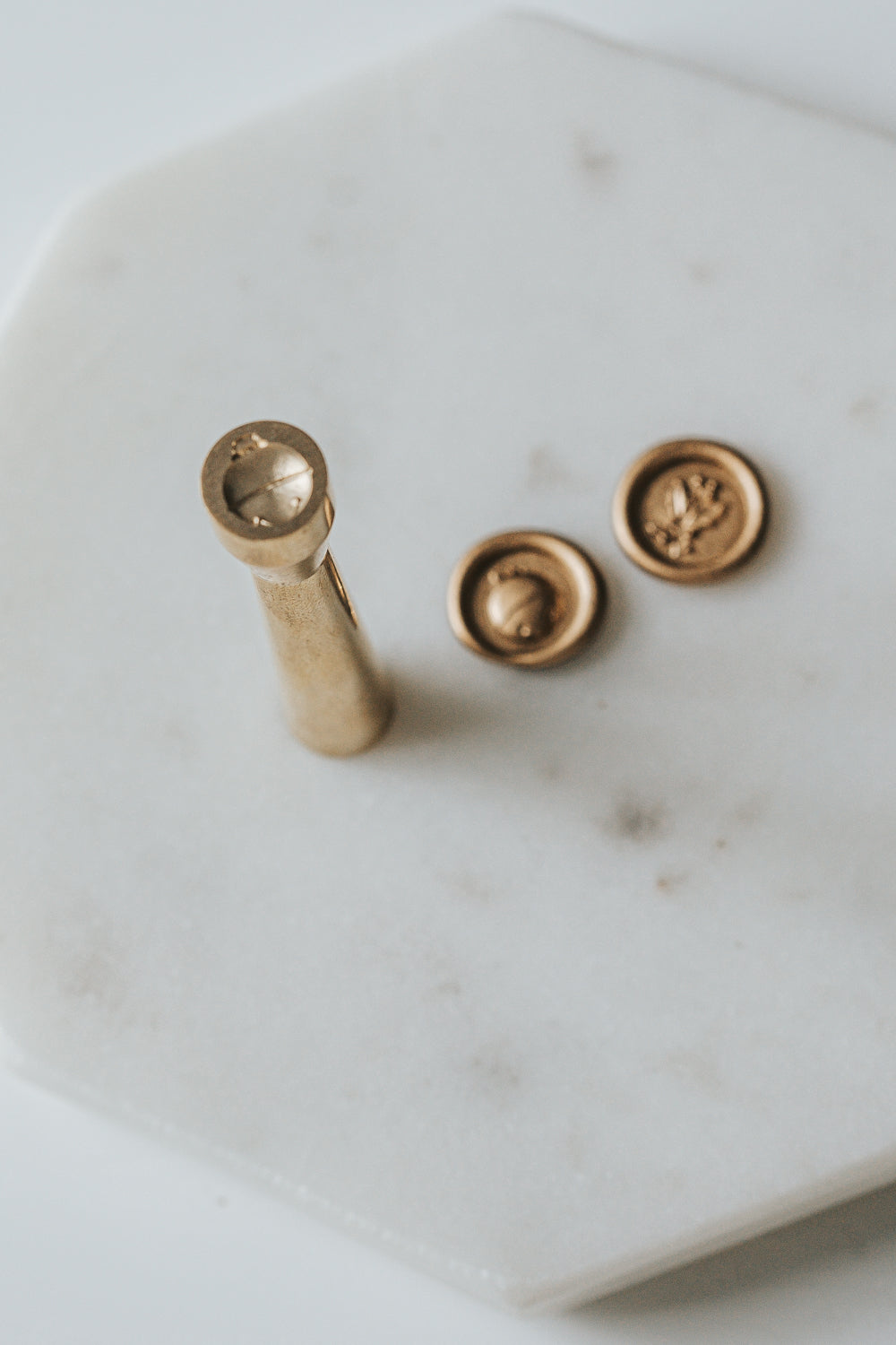 Mini wax seal stamp with a jingle bell design, displayed with matching gold wax seals on a white marble surface.