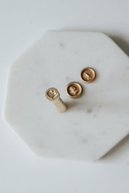 Mini wax seal stamp with a mitten design, displayed with matching gold wax seals on a white marble surface.