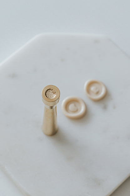 Mini wax seal stamp with a cookie design, displayed with matching beige wax seals on a white marble surface.