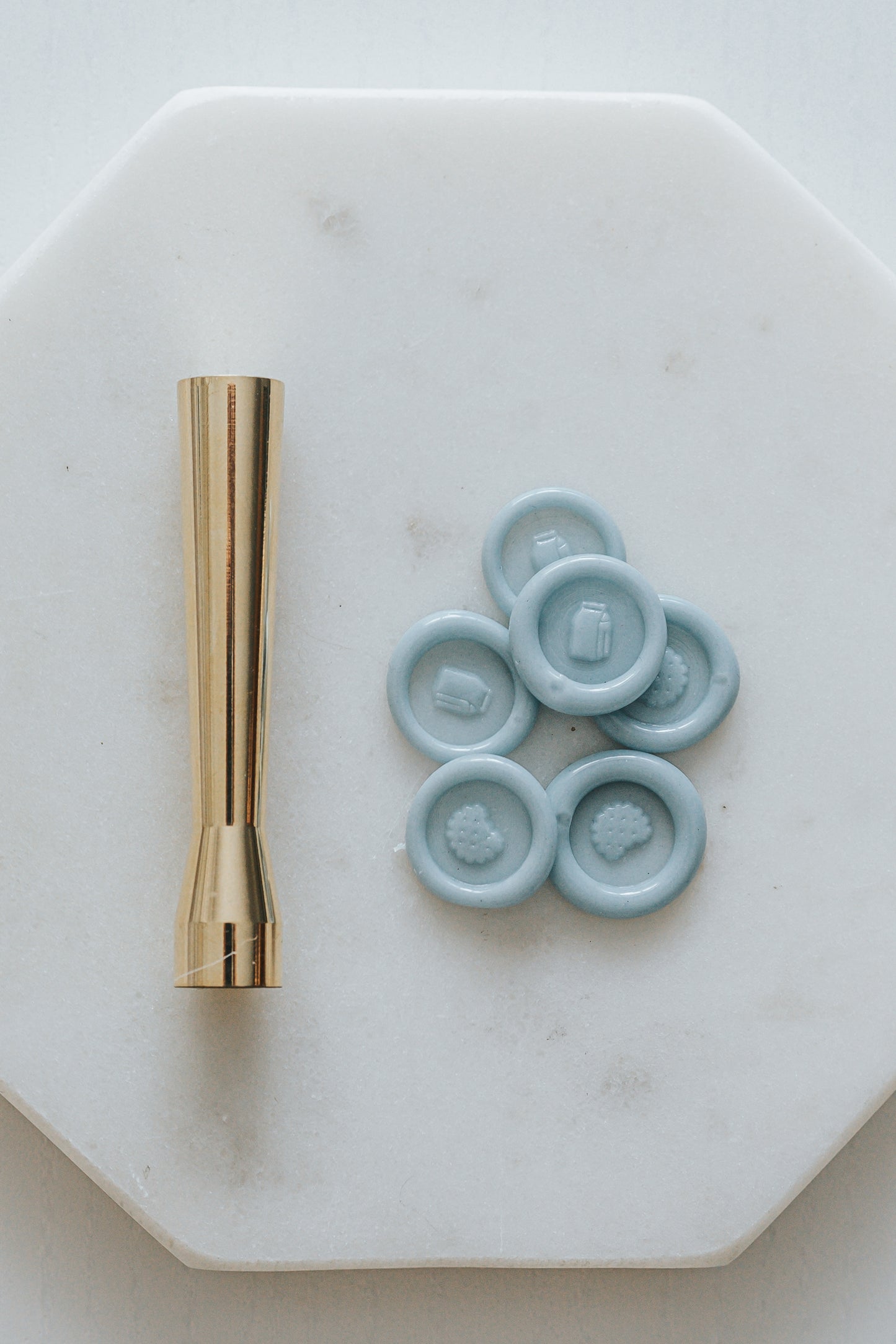 Gold miniature wax seal stamp with cookie and milk designs, placed on a white marble surface with matching blue wax seal