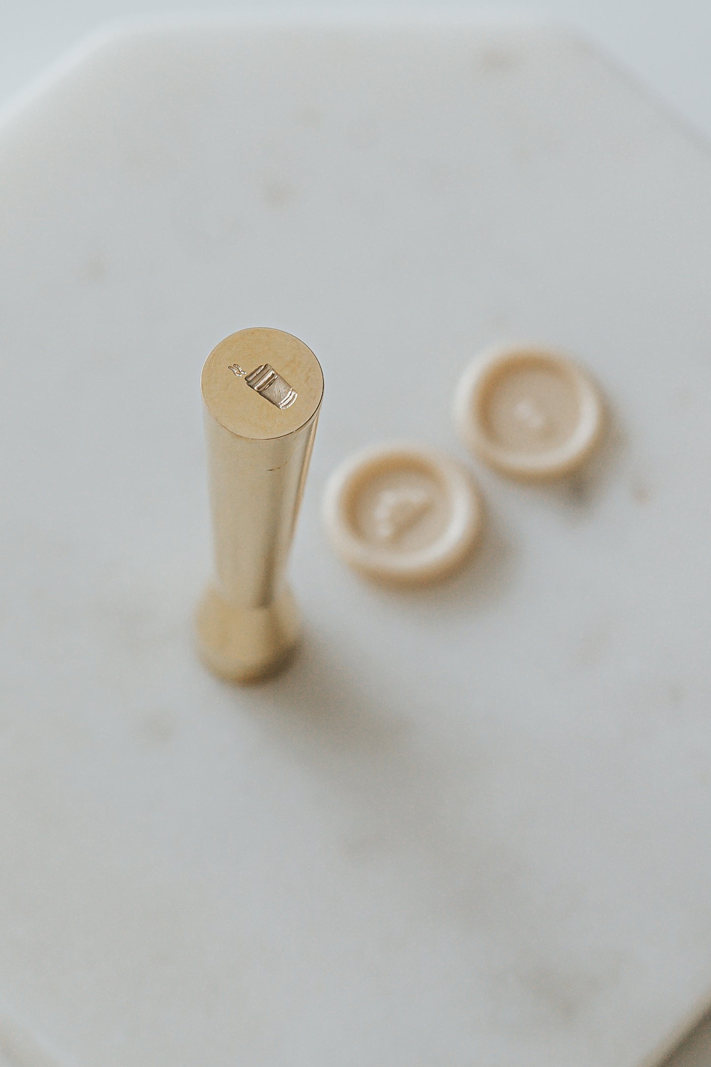 Gold miniature wax seal stamp with coffee cup designs, placed on a white marble surface with matching beige wax seal
