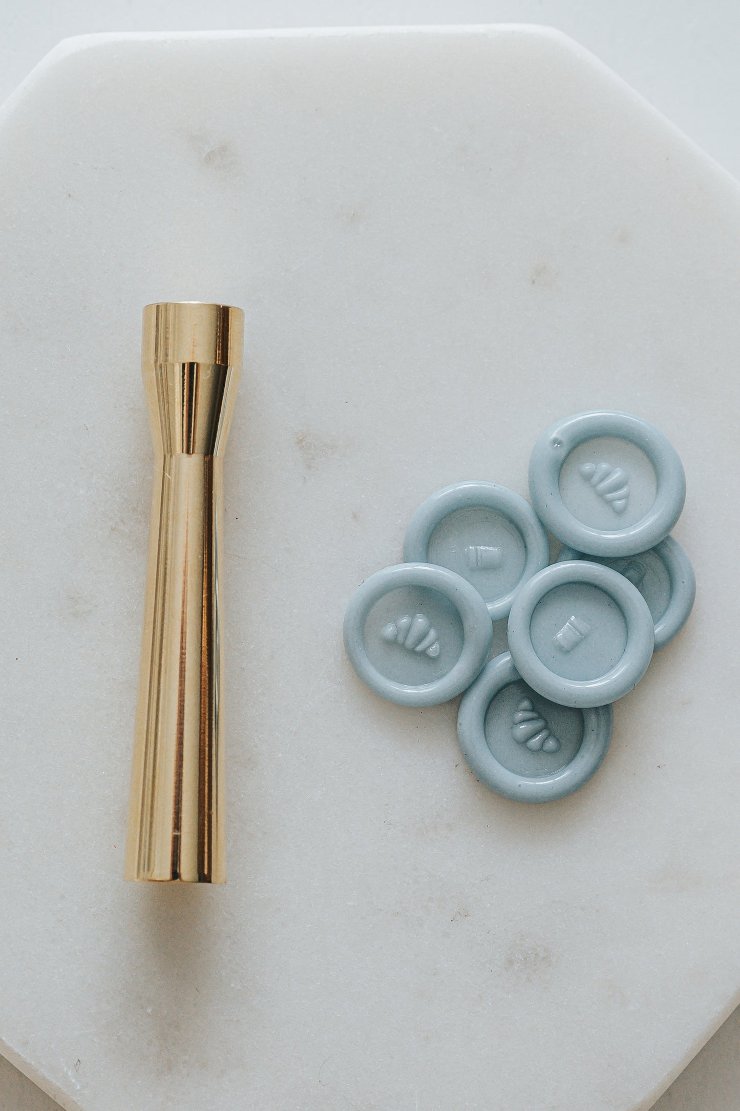 Gold miniature wax seal stamp with croissant and coffee designs, placed on a white marble surface with matching blue wax seal