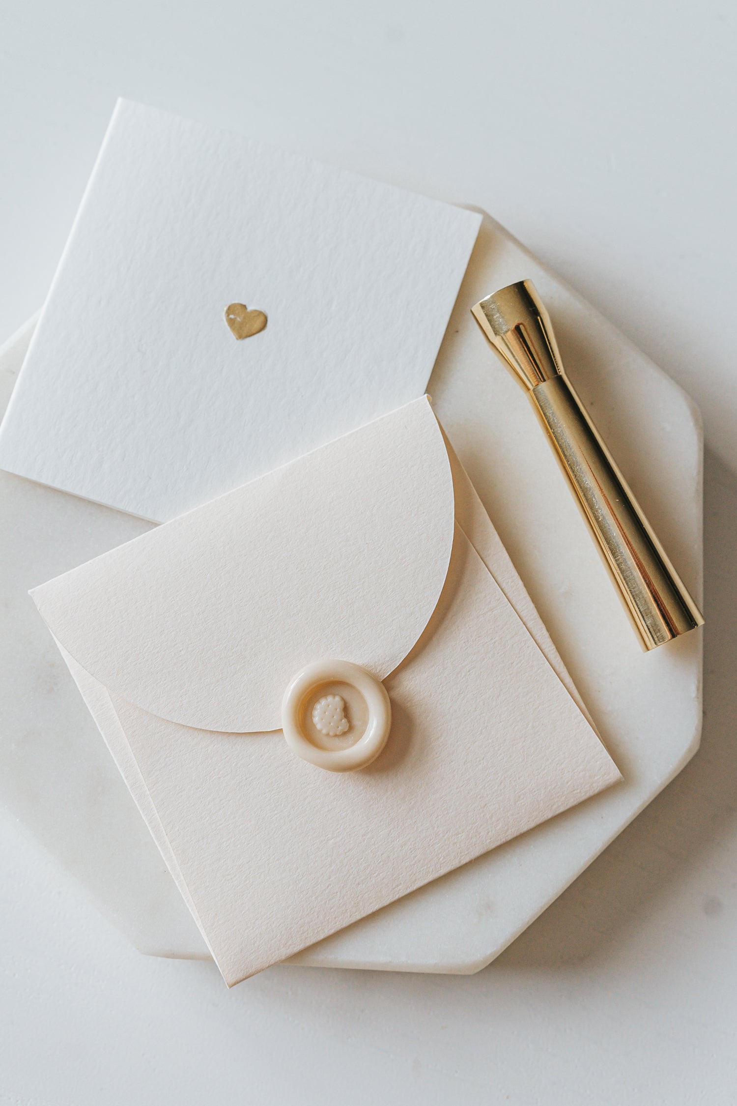 Elegant stationery with a gold heart detail and a sealed envelope, alongside a brass mini wax seal stamp on a marble plate