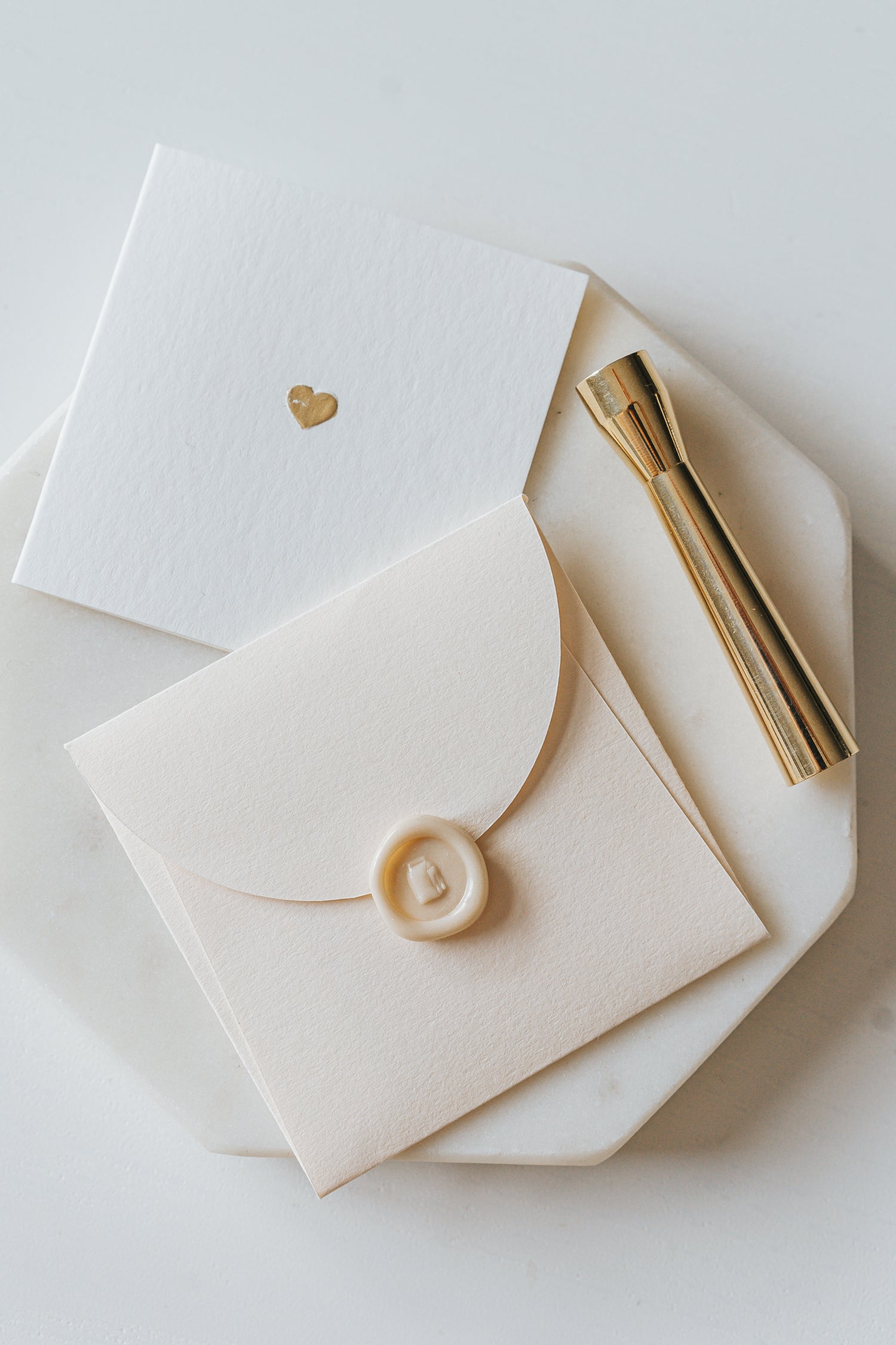 Elegant stationery with a gold heart detail and a sealed envelope, alongside a brass mini wax seal stamp on a marble plate