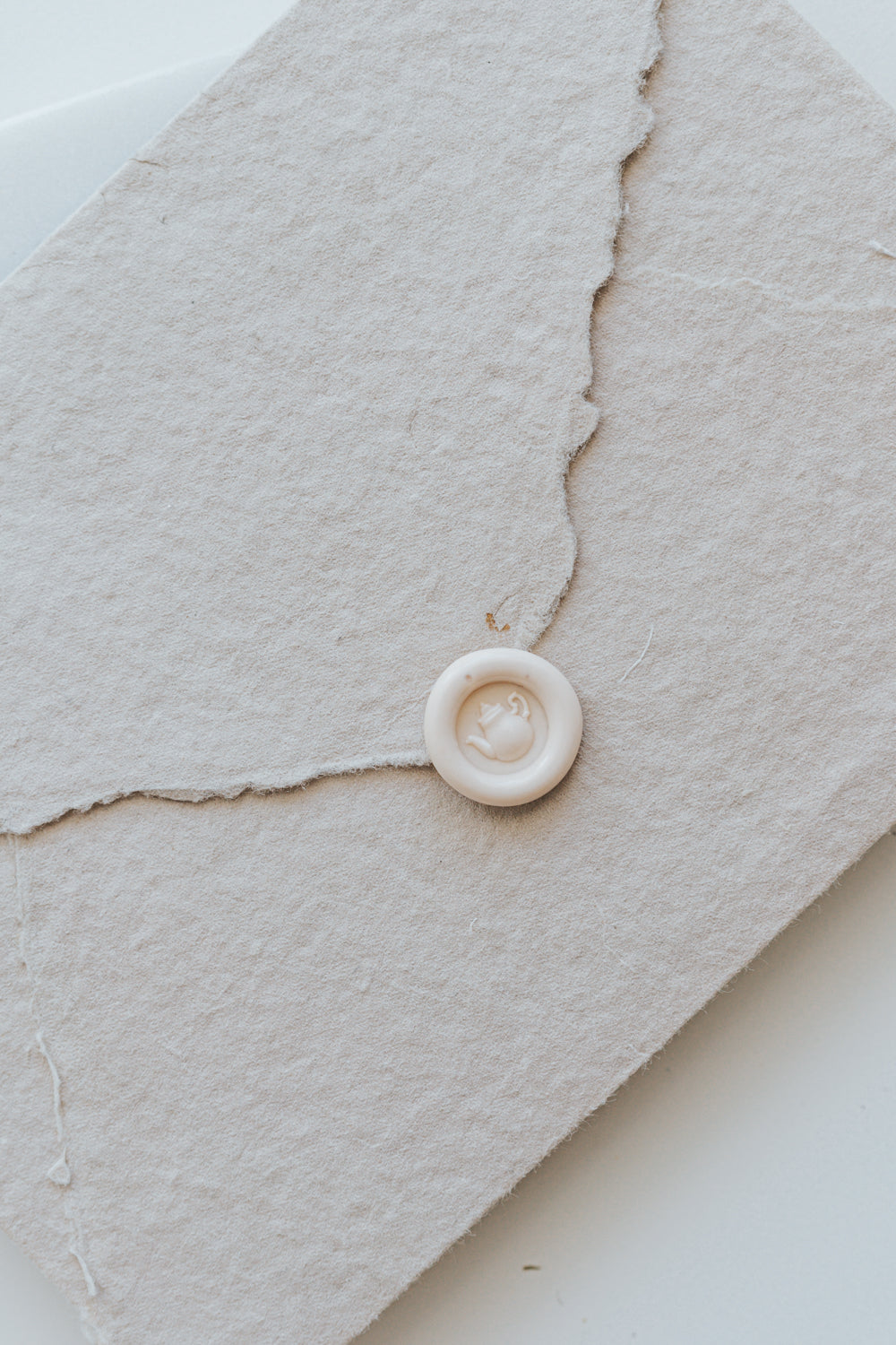 A mini 9mm blush wax seal with a 3D tea pot design on a textured taupe envelope
