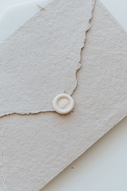 ​A mini 9mm blush wax seal with a 3D cinnamon bun design on a textured taupe envelope