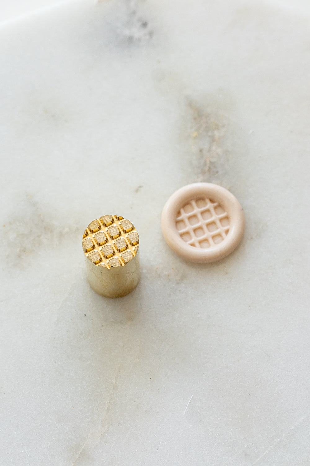 ​A mini brass wax seal stamp head with a 3D Belgian waffle design beside a blush wax seal impression on a white marble surface