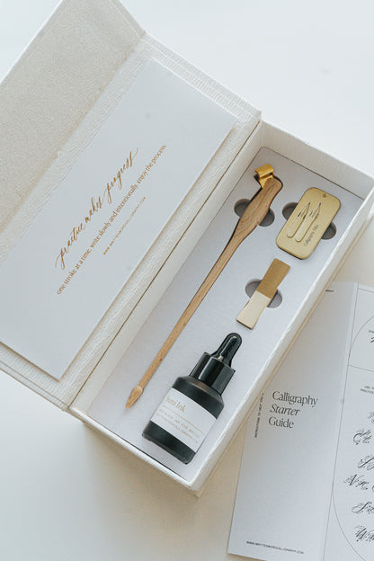 Open Mini Calligraphy Starter Kit box with sumi ink, dual-purpose pen, brass pen rest, nib tin, and guide, neatly arranged