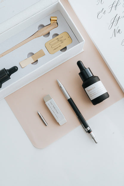 Close-up of a calligraphy starter kit featuring a wooden pen holder, sumi ink, nibs, eraser, and accessories on a desk