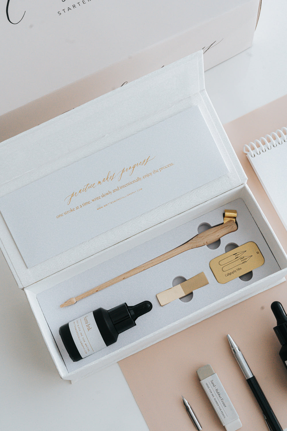 Elegant calligraphy starter kit in an open box, featuring a wooden pen holder, sumi ink, nibs, and a brass pen rest