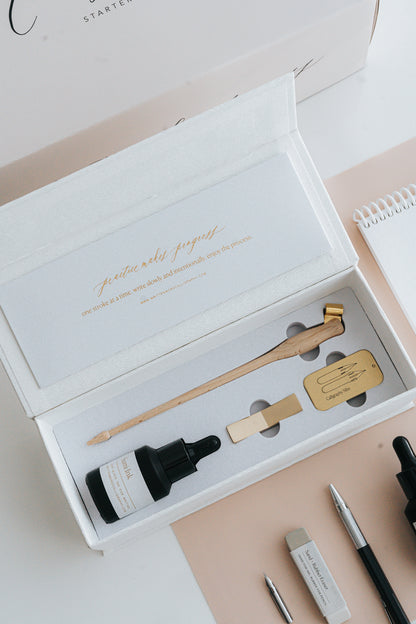 Elegant calligraphy starter kit in an open box, featuring a wooden pen holder, sumi ink, nibs, and a brass pen rest