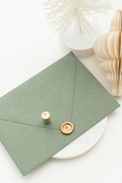 Limited edition 9mm diameter circle wax seal in gold with a 3d illustration of a wrapped present with a small ribbon bow on a green envelope.