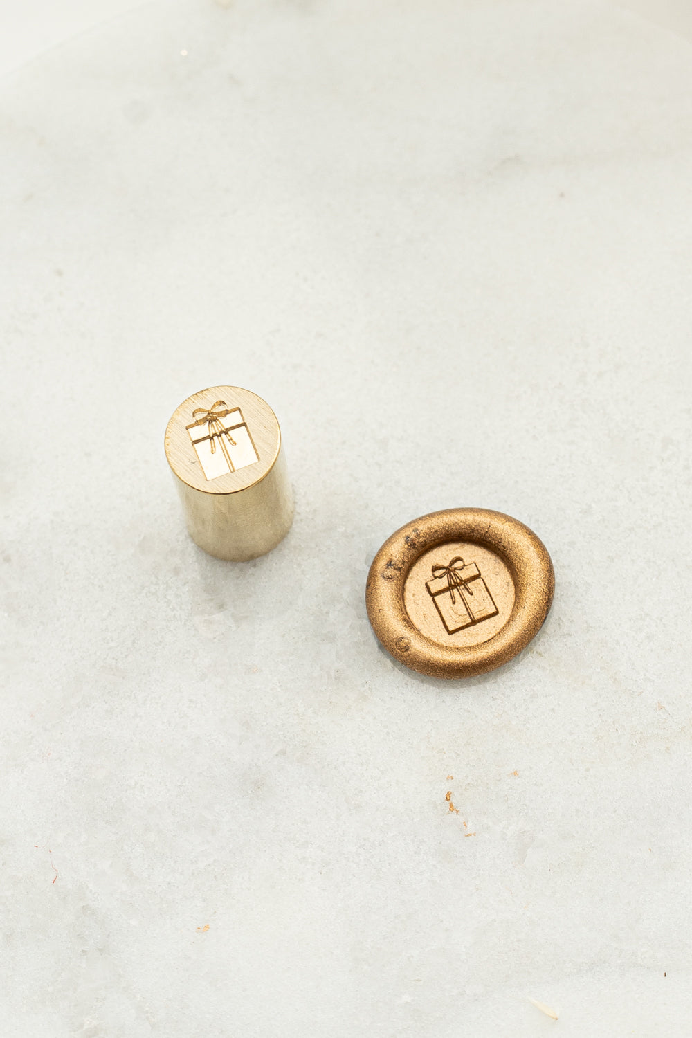 A close-up of mini wax seal stamp with a 3d illustration of a wrapped present with a small ribbon bow