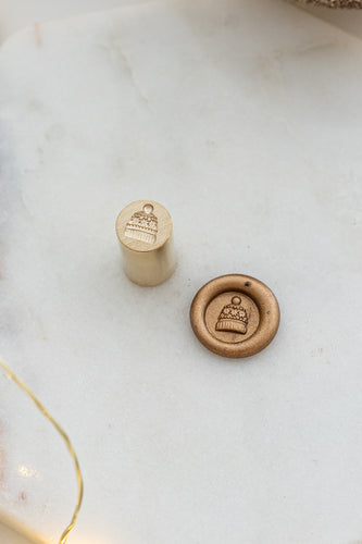Close-up of mini wax seal stamp with a cozy toque design in gold wax, part of Written Word Calligraphy’s Holiday Collection.