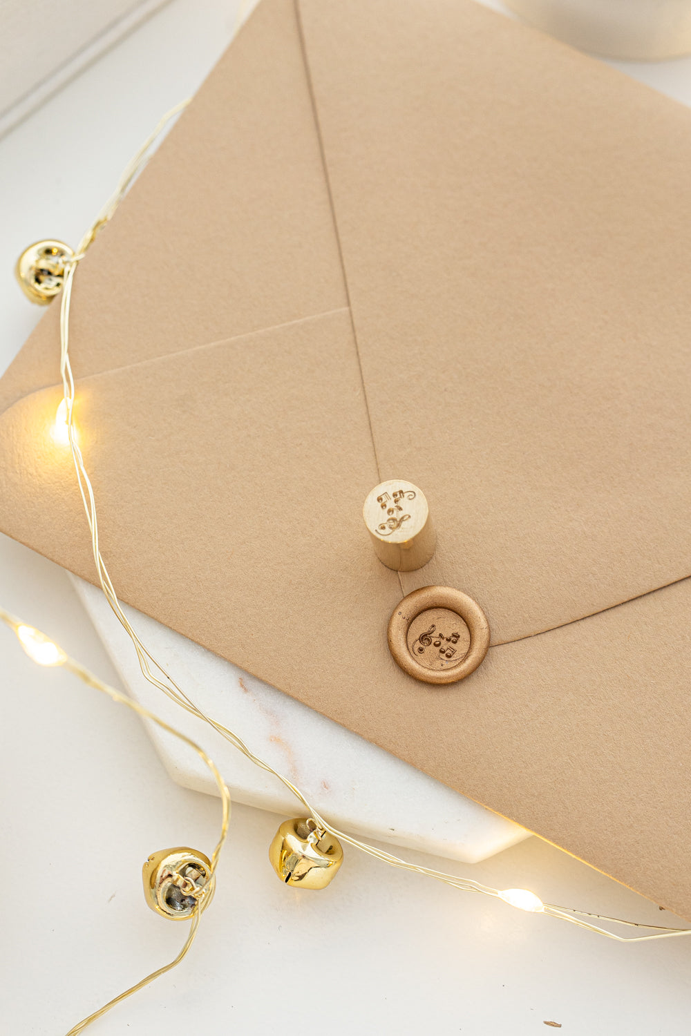 Festive mini wax seal stamp with musical notes design in gold wax on a kraft envelope, part of Written Word Calligraphy’s Holiday Collection.