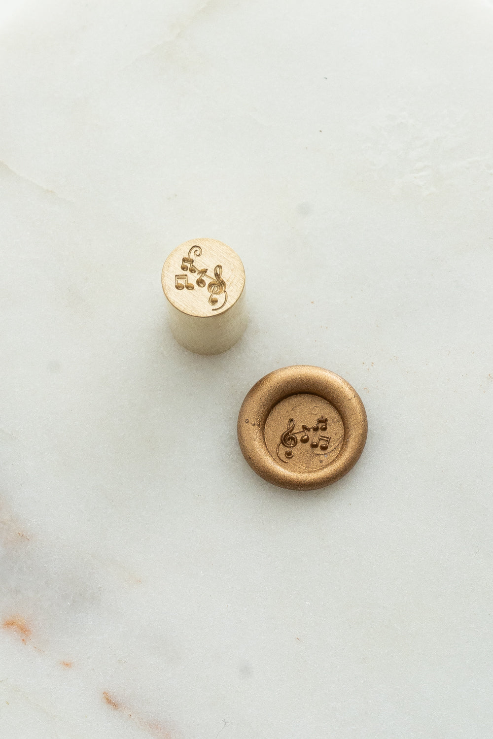Close-up of holiday wax seal stamp featuring musical notes design in gold wax, from Written Word Calligraphy’s Holiday Collection.