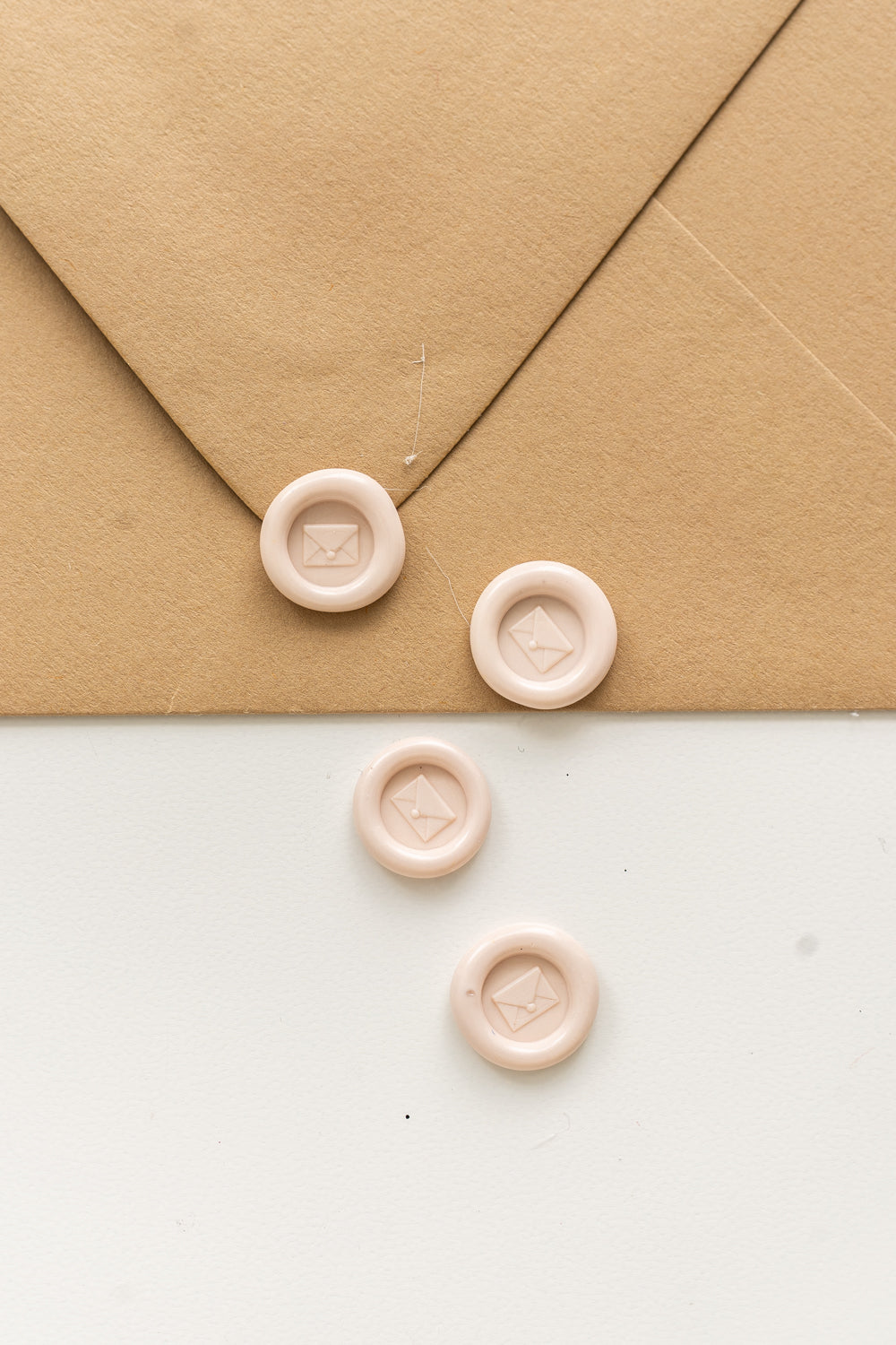 ​4 blush mini wax seals with an envelope design on a kraft envelope and white surface