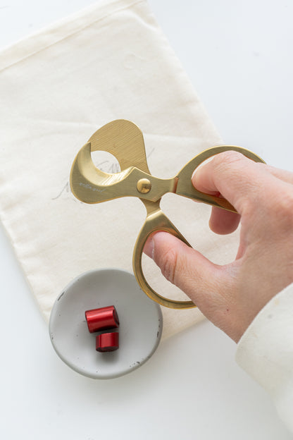 Gold wax cutter held by a hand over a small dish with cut lunar red sealing wax on a white background