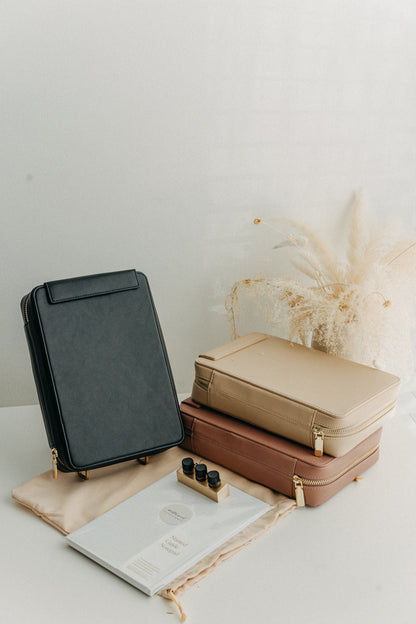 A black, beige, and dusty rose calligraphy travel case neatly arranged on a white table along with a dust bag, a notepad, and an inkwell