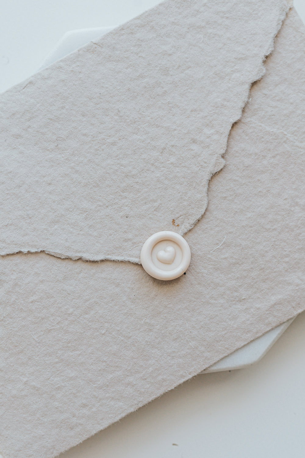 A mini 9mm blush wax seal with a 3D heart design on a textured taupe envelope