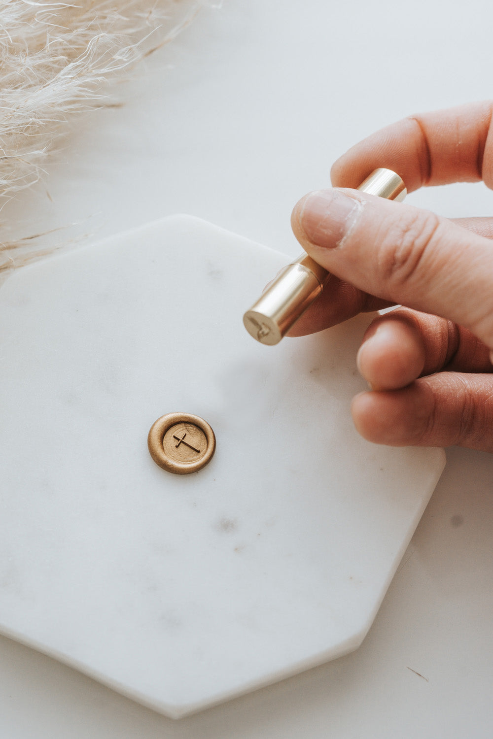 A simple cross mini brass wax seal stamp pressing a cross design into gold sealing wax 